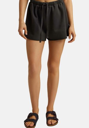 Ciemnoszare szorty z elastycznym pasem i detalem w postaci sznurka, o miękkiej, gładkiej teksturze. Połączone z czarnymi sandałami z różowymi akcentami.