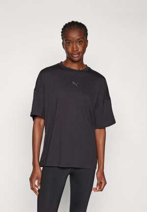 Maglietta nera oversize con maniche corte, caratterizzata da un logo discreto sul petto. Il materiale sembra morbido, con un taglio rilassato e una texture liscia.