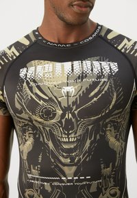 Fitted short-sleeve shirt in black and khaki, featuring a large graphic design of a skull and text. Made from stretchy, smooth fabric.