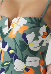 Bloemige badpak met een groene achtergrond en witte, oranje en paarse bloemen, v-hals ontwerp en dunne verstelbare straps.