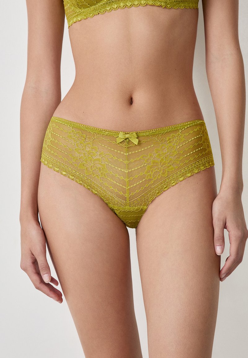 Set di biancheria intima in pizzo verde lime con motivi floreali, bordi scallop e un dettaglio a fiocco frontale. Texture morbida e trasparente in tutto il capo.