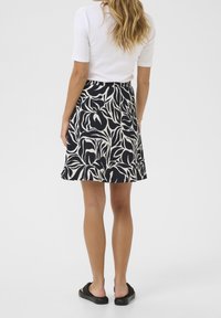 Jupe à motifs floraux noir et blanc avec une silhouette évasée, fabriquée en tissu léger, portée avec un simple haut blanc et des sandales noires.