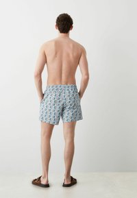 Pantaloni da bagno da uomo in azzurro chiaro con un motivo geometrico in rosso, nero e blu. Vita elastica, vestibilità comoda e due tasche laterali.