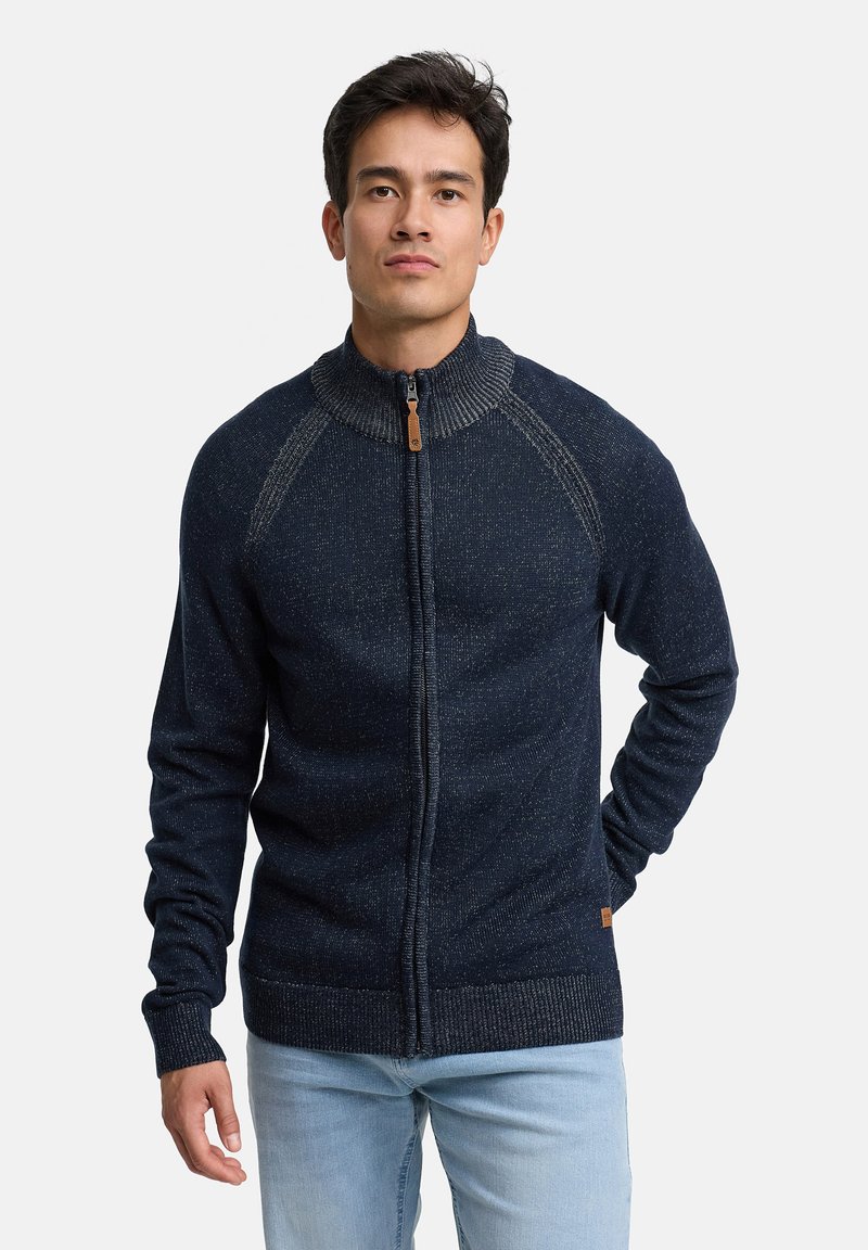 Granatowy sweter zapinany na zamek z wysokim kołnierzem, dzianą teksturą i rękawami typu raglan. Posiada mały skórzany suwak oraz ściągacze na mankietach.