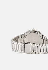 Silberne Uhr mit einem Metallarmband, rundem Gehäuse und Krone. Glatte Oberfläche, Klappverschluss und graviertes Rückendetail.