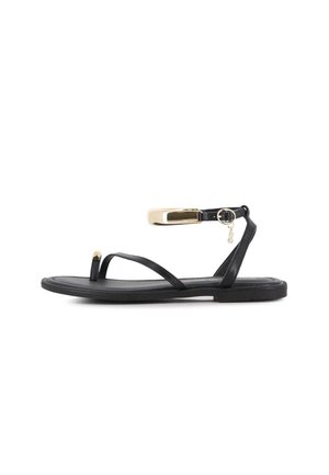 Sandalia plana negra con tiras finas, lazo para el dedo y hebilla en tono dorado en el tobillo con pequeño detalle de charm.