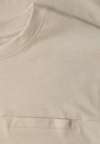 Beżowa koszulka z krótkim rękawem, z okrągłym dekoltem i małą kieszonką. Wykonana z miękkiego, gładkiego materiału o subtelnej strukturze.