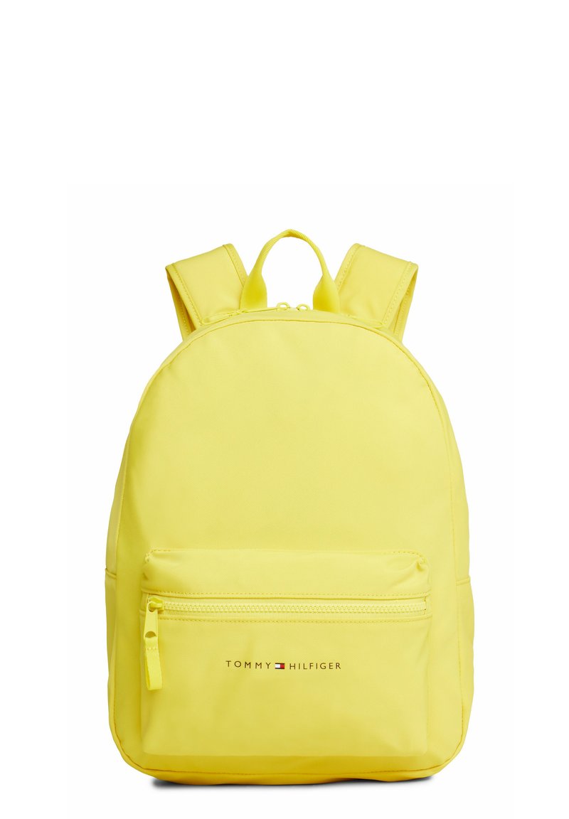 Mochila de nylon amarilla con dos correas ajustables, un bolsillo frontal con cremallera y el logo de "TOMMY HILFIGER" en la parte inferior. Textura suave.