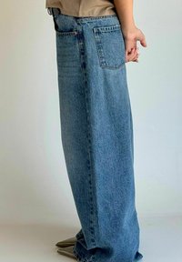 Jasnoniebieskie dżinsy o luźnym kroju, z bocznymi kieszeniami i jedną tylną kieszenią, noszone z butami o spiczastych noskach.