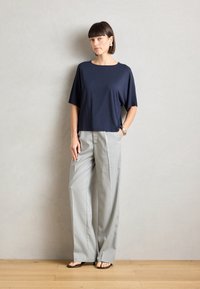 Top corto a maniche corte di colore navy abbinato a pantaloni a gamba larga a righe grigio chiaro. Il modello è in piedi su un pavimento in legno di fronte a una parete texturizzata.