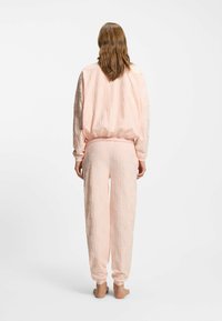 Lichtroze bijpassende loungewear-set met een gestructureerd ontwerp met "hug"-motieven, elastische manchetten en een ontspannen pasvorm voor zowel top als broek.