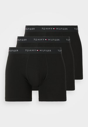 Três boxers pretos da Tommy Hilfiger empilhados, cada um com uma cintura elástica de marcação que apresenta o logótipo e o emblema da bandeira.