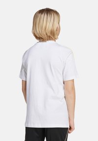Witte katoenen t-shirt met een ronde halslijn, korte mouwen en een eenvoudige achterkant; heeft een subtiele gele accent op de schouder.