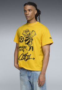 Gul bomulds t-shirt med et sort grafisk motiv af en bi med en fodbold. Korte ærmer, afslappet pasform og rund hals.