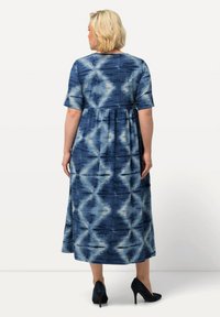 Maxiklänning i mörkblått och ljusblått batikmönster, korta ärmar och en avslappnad överdel med samlad midja. Bärs med mörka klackar.