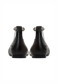Bailarinas de cuero negro con un tacón bajo, que cuentan con un detalle de cadena en la parte trasera, acentos decorativos y una textura suave y pulida.