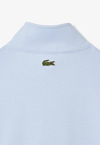 Polo shirt azzurro chiaro con colletto a costine e logo di coccodrillo verde ricamato sulla schiena. La trama del tessuto è liscia e morbida.