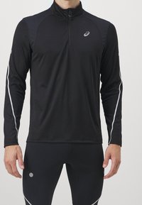 Czarna, długosleeve'owa koszulka sportowa z kołnierzem na zamek błyskawiczny, z odblaskowymi srebrnymi paskami wzdłuż rękawów i logo na piersi.