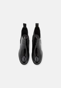 Botines de charol negro con paneles laterales elásticos y tiradores. Textura suave y diseño de punta redonda. Suela de goma.