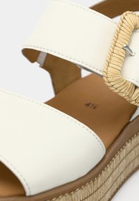 Λευκό δερμάτινο σανδάλι με φαρδιά λουρί, υφαντή λεπτομέρεια και σόλα πλατφόρμας από φυσικές ίνες. Λείο υφή και ελαφριά λάμψη στην επιφάνεια.