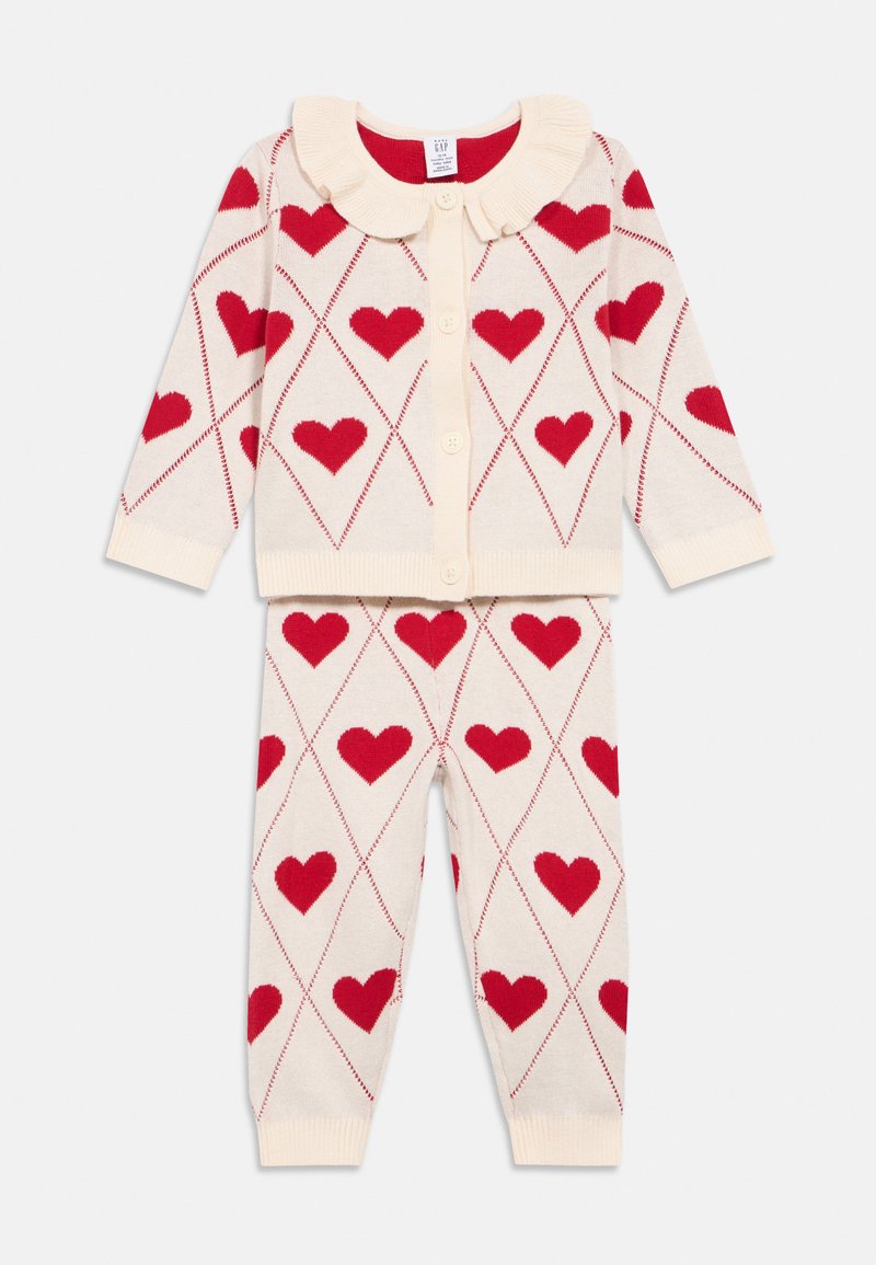 Krémově zbarvený pletený dvoudílný set obsahující kardigan se volánkovým límcem, červenými vzory srdcí a odpovídající kalhoty s manžetami.