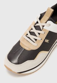 Baskets noires, beiges et blanches avec détails en mesh et en daim, lacets blancs et logo métallique « MK » sur le côté.