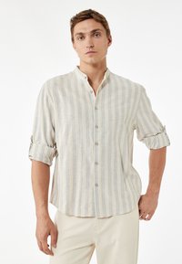 Button-up skjorte i lys beige med blå striber; blanding af linned, afslappet pasform, kravefri design, oprullede ærmer, subtil tekstur.