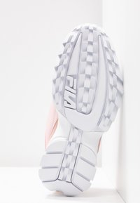 Semelle d'une basket FILA blanche et rose montrant un motif d'adhérence texturé et le logo de la marque sur un fond blanc propre.