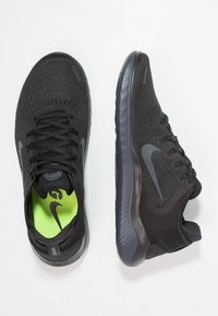 Baskets de sport noires avec un dessus en maille texturée, accents gris et semelle intérieure verte fluo. Semelle arrondie pour flexibilité et confort.