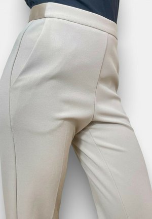 Primo piano di pantaloni beige a vita alta su misura con tasche laterali indossati con un top scuro, che mostrano un tessuto liscio e una vestibilità aderente.