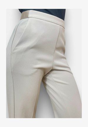 Primo piano di pantaloni beige a vita alta su misura con tasche laterali indossati con un top scuro, che mostrano un tessuto liscio e una vestibilità aderente.