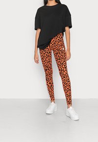 T-shirt noir surdimensionné associé à des leggings à motif léopard orange avec des bandes latérales blanches, et des baskets plateformes blanches.