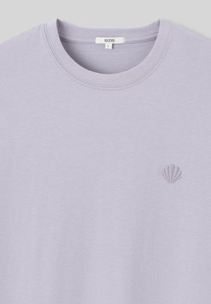 T-shirt lilas clair avec un col ras du cou, ornée d'un petit design de coquillage brodé sur la poitrine. Texture douce, coupe d écontractée.