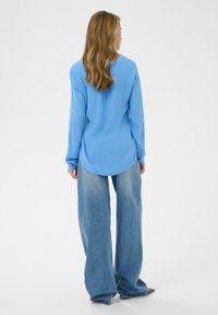 Chemise à manches longues bleu clair avec un col rond, associée à un jean bleu à jambes larges, caractérisée par une coupe décontractée et une texture douce.