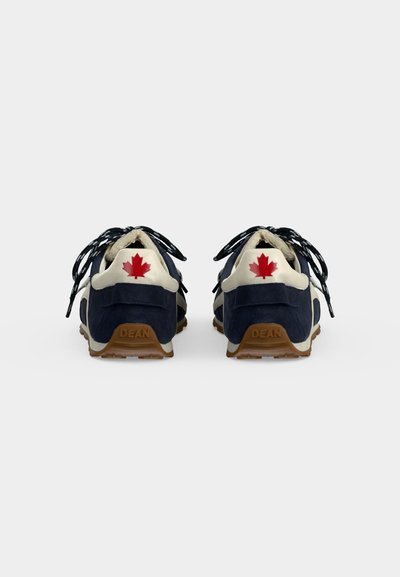 Paire de baskets bleu marine et blanches avec des lacets noirs, avec des logos de feuille d'érable rouge et le mot "DEAN" sur des semelles marron, vues de dos.