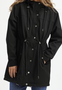Giacca softshell nera con cappuccio, vita regolabile con coulisse, bottoni a pressione e tasche laterali. Texture liscia, design casual.