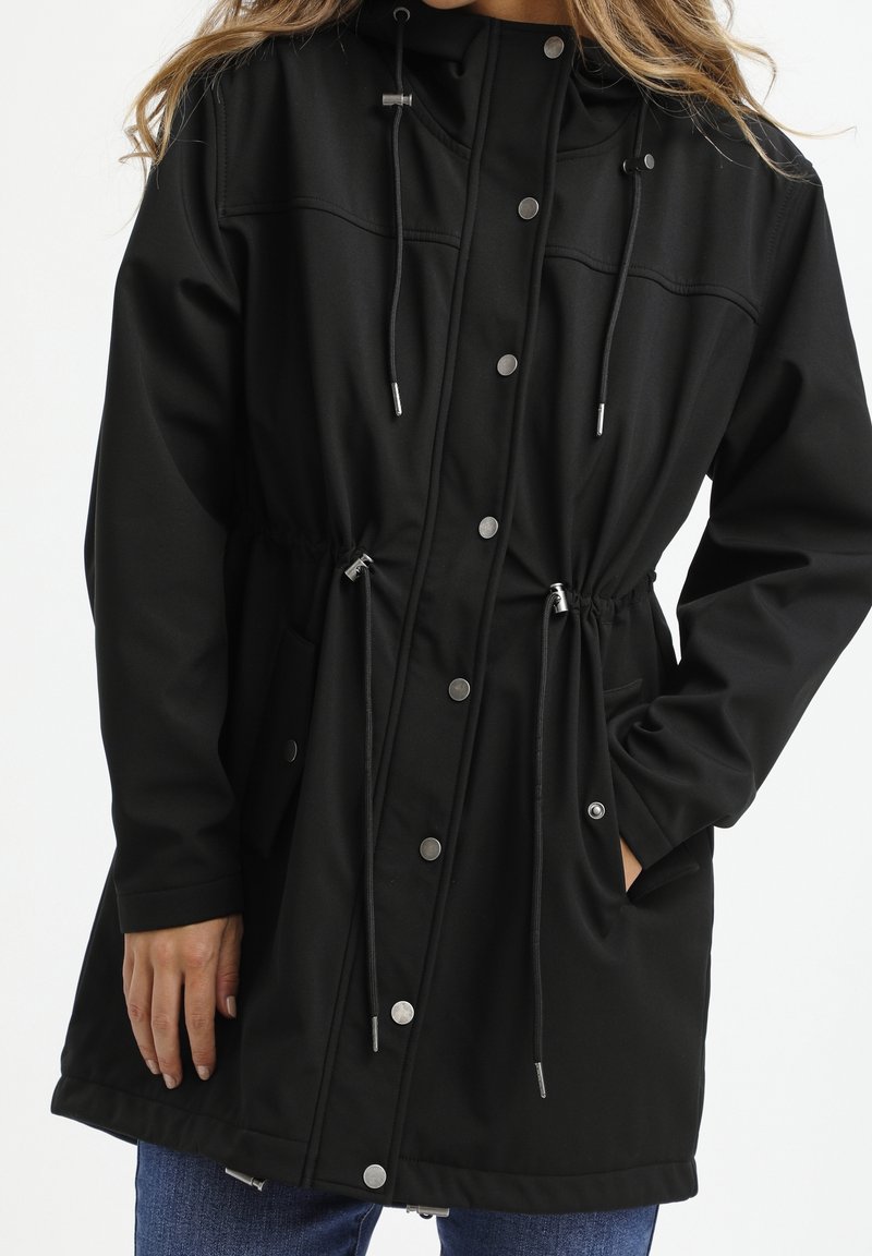 Giacca softshell nera con cappuccio, vita regolabile con coulisse, bottoni a pressione e tasche laterali. Texture liscia, design casual.