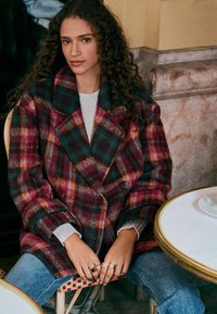 Ruuduline villane mantel punastes, rohelistes ja roosades toonides. Notšitud krae, kahekordne disain. Stiliseeritud heleda sviitriga ja sõrmustega.