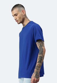 T-shirt blu a maniche corte con scollatura rotonda, realizzato in un tessuto morbido. Caratterizzato da una vestibilità comoda e tatuaggi visibili sul braccio del modello.