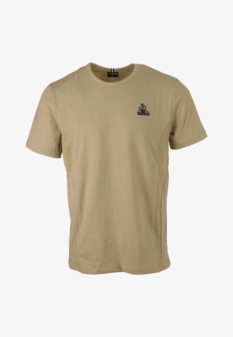T-shirt corto a maniche corte di colore tan, realizzato in cotone con pannelli laterali in rete. Presenta un piccolo logo nero sul lato sinistro del petto e un collo a costine.