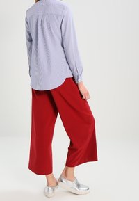 Blue and white striped long-sleeve shirt, red wide-leg pants, silver slip-on shoes. Smooth fabric, relaxed fit, and buttoned cuffs.