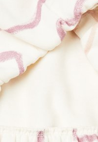 Tela multicolorida con un fondo crema y líneas onduladas rosas. Textura suave, con un detalle de borde gathered y elástico.
