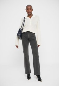 Jeans neri a gamba dritta abbinati a un top in maglia crema testurizzata con colletto. Gli accessori includono una borsa blu navy e stivali neri con tacco.
