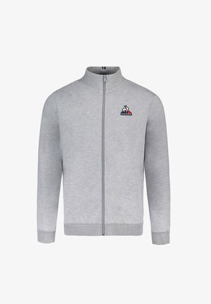 Sudadera gris con cremallera y cuello alto, puños acanalados y cinturilla elástica. Presenta un pequeño logo en el lado izquierdo del pecho. Textura suave.