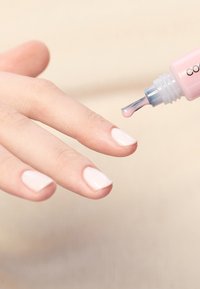 Nagellakapplicator met een platte punt die lichte roze nagellak aanbrengt op een hand met korte, netjes verzorgde witte nagels.