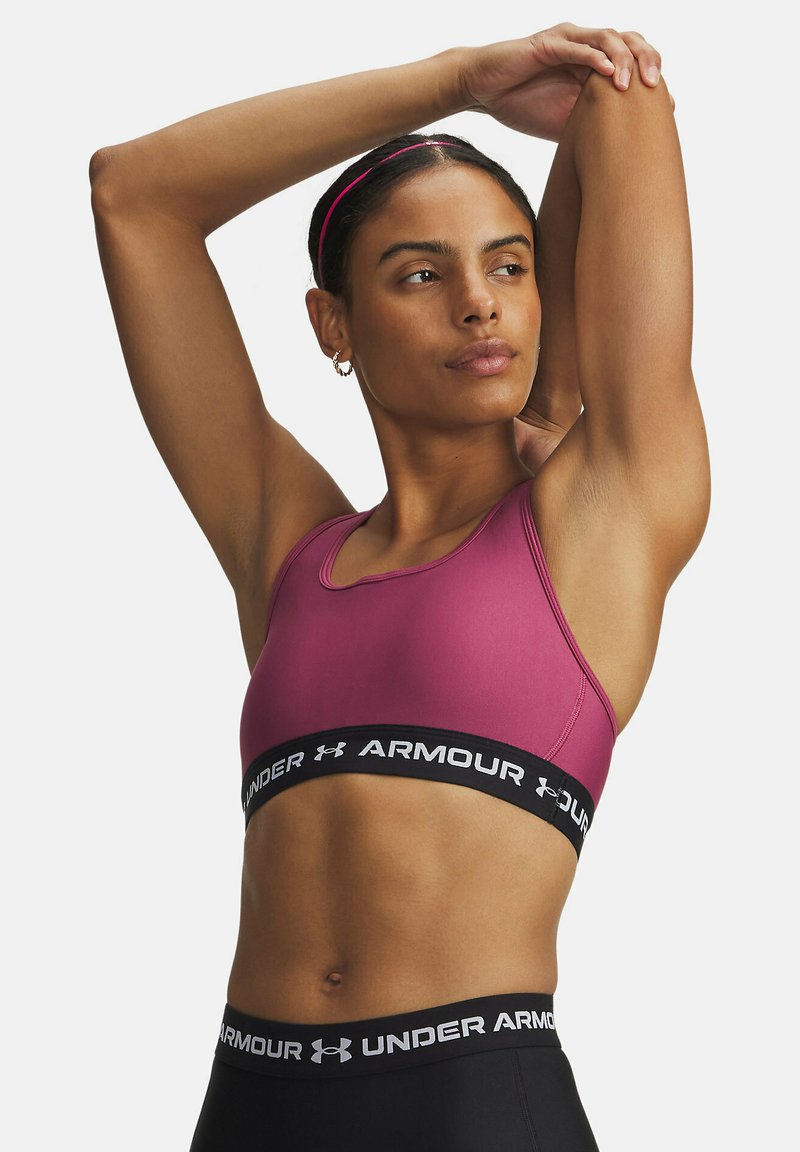 Roze sportbh gemaakt van rekbaar materiaal, met een zwarte elastische band met merknaam onderaan. Ontworpen voor comfort en ondersteuning tijdens activiteiten.