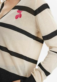 Knit sweater featuring beige and black horizontal stripes, a v-neck, and pink embroidered leaf detail on the left side. Long sleeves.