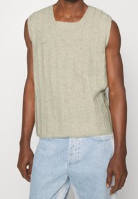 Maglione senza maniche di colore verde chiaro lavorato a maglia con righe verticali e un ampio scollo rotondo, abbinato a jeans in denim blu chiaro.