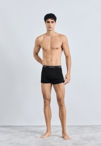 Boxers de tela negra con una cinturilla de altura media que presenta un logo blanco. El diseño es simple, sin patrones ni acentos.