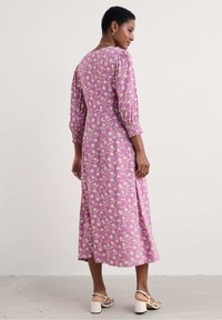 Lång rosa klänning med lövmönster, med puffärmar och insydd midja. Slät tyg, ankellång, kompletterad med klacksandaler.
